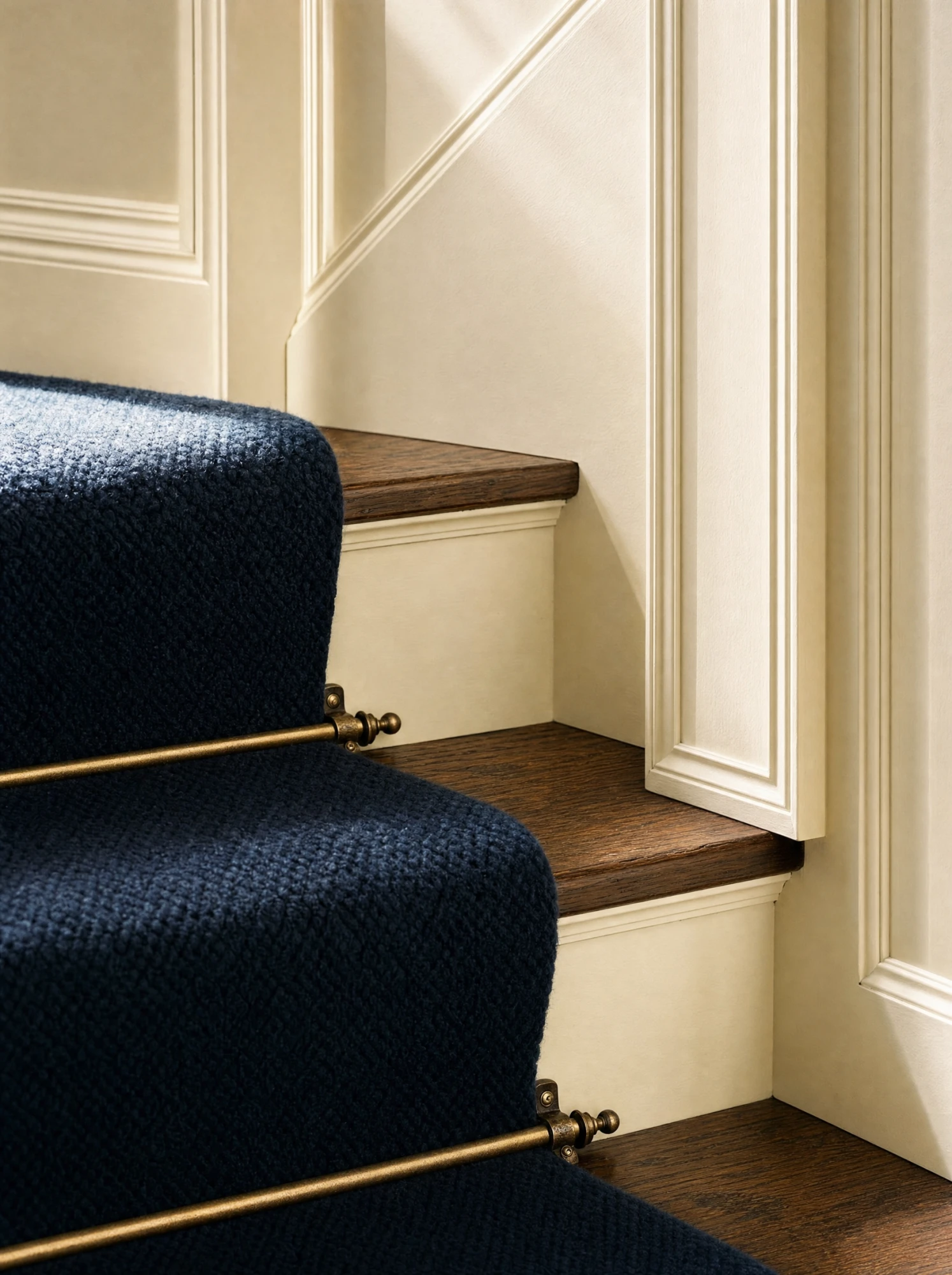 Brass stair rods over the navy runner on dark-oak treads